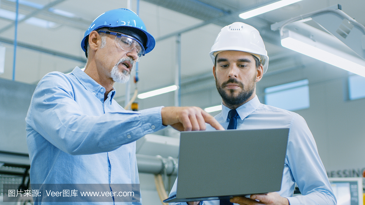 部門主管持有筆記本電腦并與總工程師討論產(chǎn)品細(xì)節(jié)。他們戴著安全帽在現(xiàn)代工廠工作。